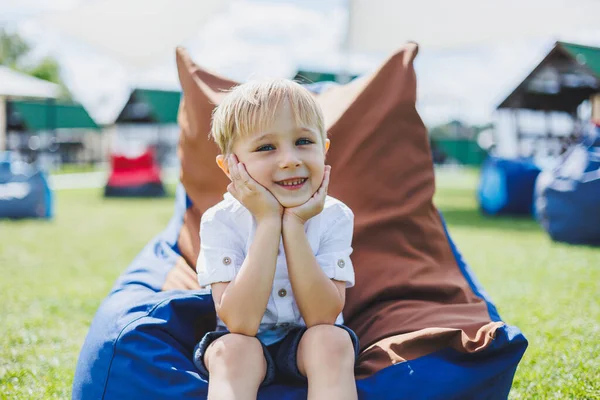 Mutlu çocuk yaz parkında koltukta oturuyor. Beyaz tişörtlü küçük bir çocuk dışarıda eğleniyor. Çocukluk ve mutluluk.