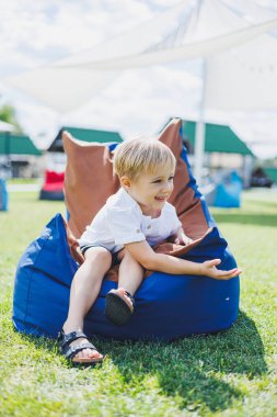 Mutlu çocuk yaz parkında koltukta oturuyor. Beyaz tişörtlü küçük bir çocuk dışarıda eğleniyor. Çocukluk ve mutluluk.