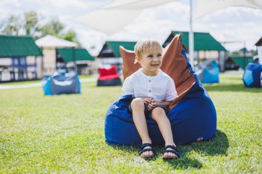Mutlu çocuk yaz parkında koltukta oturuyor. Beyaz tişörtlü küçük bir çocuk dışarıda eğleniyor. Çocukluk ve mutluluk.