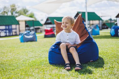 Mutlu çocuk yaz parkında koltukta oturuyor. Beyaz tişörtlü küçük bir çocuk dışarıda eğleniyor. Çocukluk ve mutluluk.