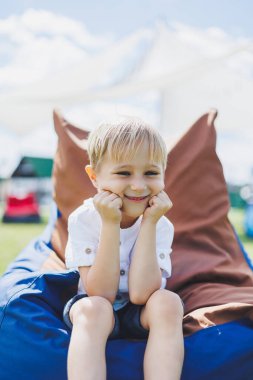 Mutlu çocuk yaz parkında koltukta oturuyor. Beyaz tişörtlü küçük bir çocuk dışarıda eğleniyor. Çocukluk ve mutluluk.