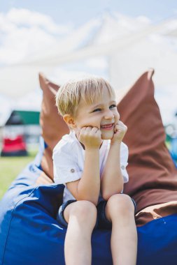 Mutlu çocuk yaz parkında koltukta oturuyor. Beyaz tişörtlü küçük bir çocuk dışarıda eğleniyor. Çocukluk ve mutluluk.
