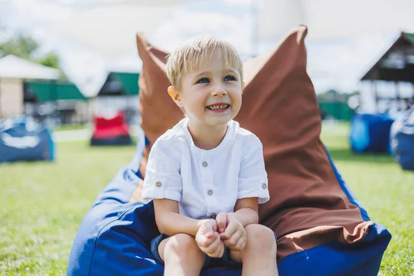 Mutlu çocuk yaz parkında koltukta oturuyor. Beyaz tişörtlü küçük bir çocuk dışarıda eğleniyor. Çocukluk ve mutluluk.