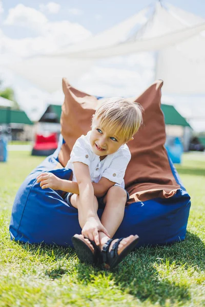 Mutlu çocuk yaz parkında koltukta oturuyor. Beyaz tişörtlü küçük bir çocuk dışarıda eğleniyor. Çocukluk ve mutluluk.