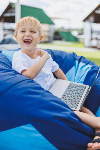 A cheerful child is playing on colorful beanbag chairs on the street. A little boy watches cartoons on a laptop while sitting on a chair in the park