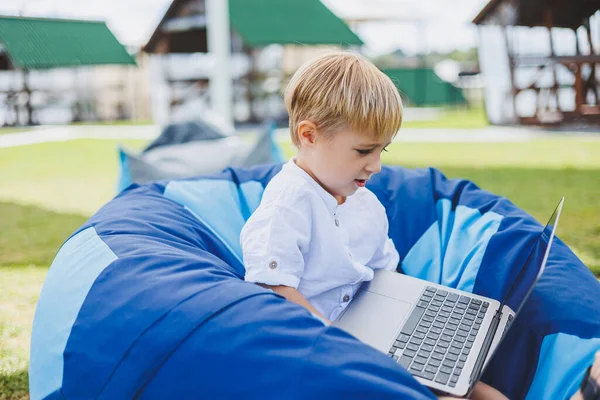 A cheerful child is playing on colorful beanbag chairs on the street. A little boy watches cartoons on a laptop while sitting on a chair in the park