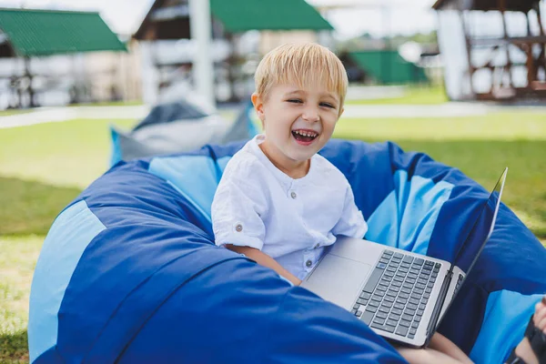 A cheerful child is playing on colorful beanbag chairs on the street. A little boy watches cartoons on a laptop while sitting on a chair in the park