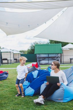 Küçük çocuk yazın ya da ilkbaharda açık havada yatakta otururken eğleniyor. Anne ve oğlunun temiz havada geçirdiği aile tatili