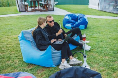 Genç bir çift parkta rahatlıyor ve nargile içiyor. Bir erkek ve bir kadın doğada sandalyede oturup nargile içerler. Aile tatili