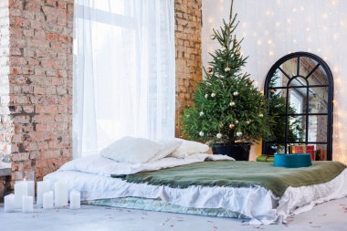 Yılbaşı hediyeleri kağıtta ve yılbaşı arifesinde yerde, Noel ağacının altında parlak kurdeleler. Oyuncaklarla süslenmiş bir Noel ağacı yatağın yanında duruyor.