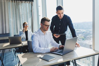 Modern ofis. Genç iş adamları resmi olarak proje detaylarını tartışıyor ve modern yönetim kurulunda iş birliği yaparken dizüstü bilgisayarın ekranına bakıyor..