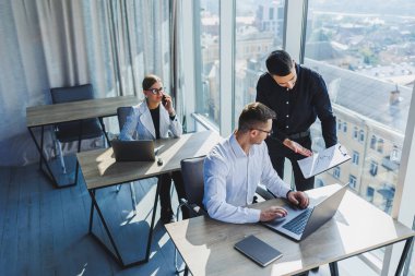 Modern ofis. Genç iş adamları resmi olarak proje detaylarını tartışıyor ve modern yönetim kurulunda iş birliği yaparken dizüstü bilgisayarın ekranına bakıyor..