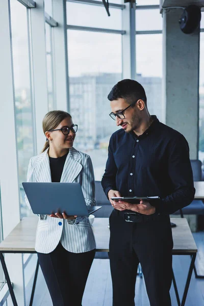 Beautiful businesswoman standing with Caucasian male colleague watching laptop screen and talking with businessman in office. Business relations between colleagues