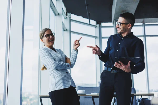 Positive businesswoman standing with Caucasian male colleague talking to businessman in office. Business relations between colleagues with smiles in a warm atmosphere