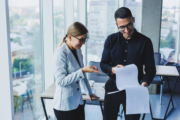 Positive businesswoman standing with Caucasian male colleague talking to businessman in office. Business relations between colleagues with smiles in a warm atmosphere