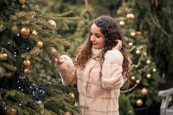 코트를 곱슬머리의 여자가 크리스마스 박람회를 거닐고 있습니다 크리스마스와 새해를 기다리며 — 스톡 사진