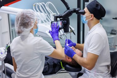 Bir dişçi ve bir asistan bir hastanın dişlerini mikroskop kullanarak tedavi eder. Profesyonel diş temizliği. Diş hekimliği. Diş mikroskobu.