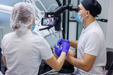 Bir dişçi ve bir asistan bir hastanın dişlerini mikroskop kullanarak tedavi eder. Profesyonel diş temizliği. Diş hekimliği. Diş mikroskobu.