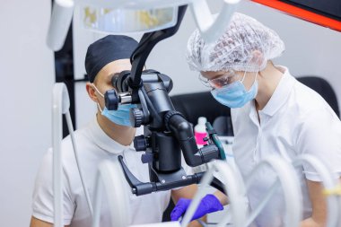 Diş hekimi ve asistanı, dişçi muayenehanesinde hastanın dişlerini mikroskop, ayna ve sonda ile kontrol ediyor. Tıp, dişçilik ve sağlık sigortası kavramı. Diş ekipmanları