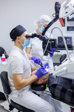 Diş hekimi ve asistanı, dişçi muayenehanesinde hastanın dişlerini mikroskop, ayna ve sonda ile kontrol ediyor. Tıp, dişçilik ve sağlık sigortası kavramı. Diş ekipmanları
