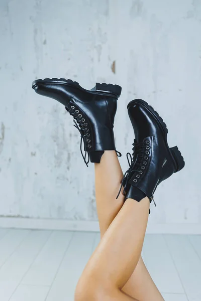 Female legs in leather black autumn boots. A fashion girl stands in a store and measures shoes.