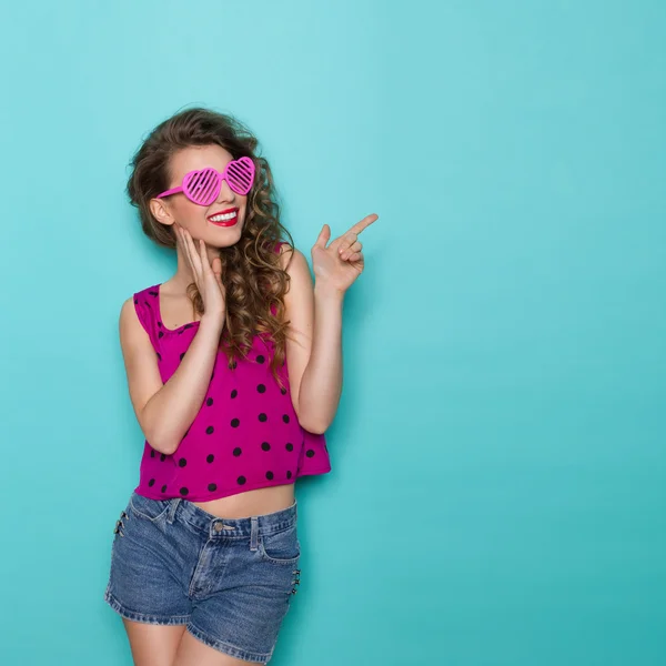 Smiling girl in heart shaped glasses is pointing