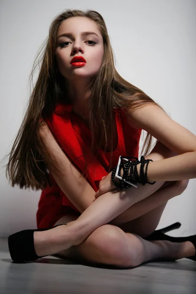 Woman in red dress sitting on floor with crossed legs — Stock Photo, Image