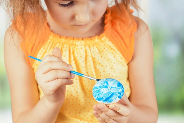 Girl paints Easter egg in blue color — Stock Photo, Image