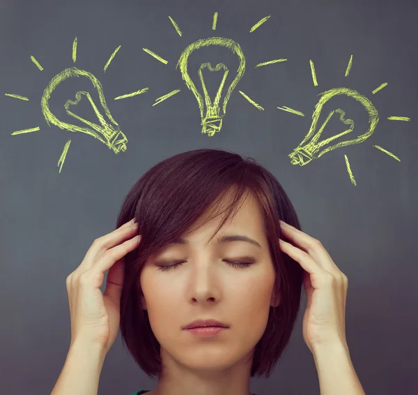Woman touches her head on a background of light bulbs — Stock Photo, Image