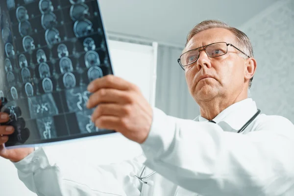 Older doctor examines MRI image — Stock Photo, Image