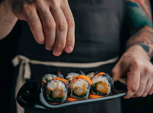 El hombre espolvorea especias en rollos de sushi para servir el plato. — Foto de Stock