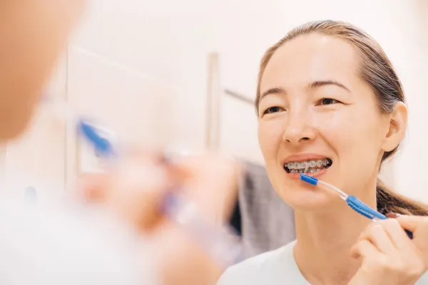 Mujer joven con aparatos ortopédicos limpia sus dientes con un cepillo dental especial, ante el espejo. — Foto de Stock