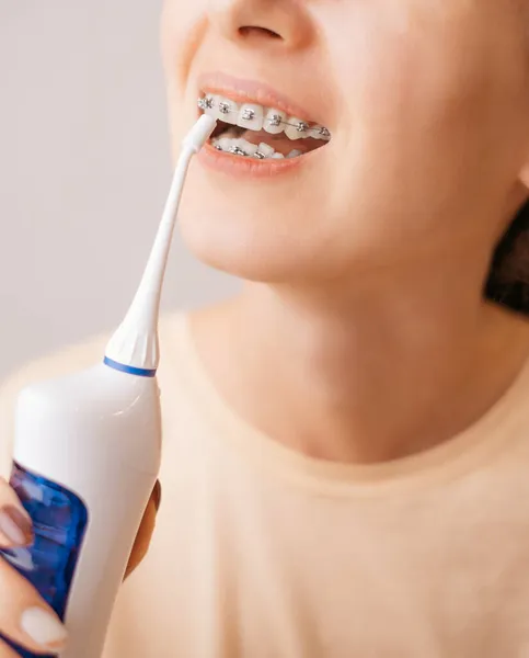 Mujer lavando un aparato ortopédico con un irrigador para la salud dental. — Foto de Stock