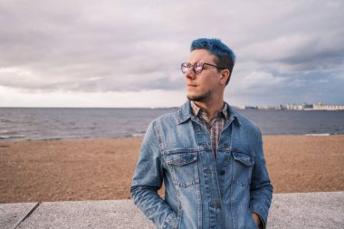 Mavi saçlı genç bir adam gün batımında setin kenarında duruyor..