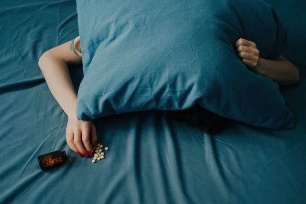 A young woman lies on the bed with her head under the pillow. — Stock Photo, Image