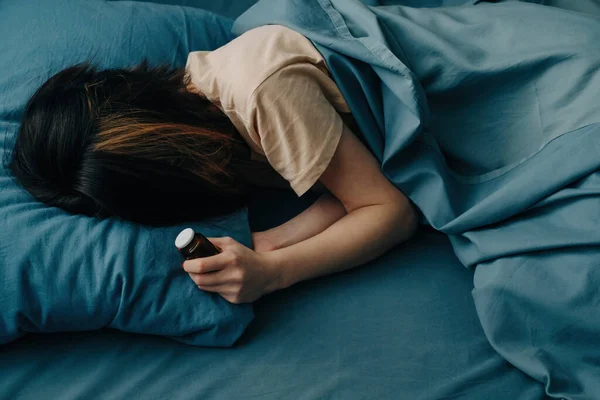 Ung kvinna i sängen med antidepressiva piller i händerna. — Stockfoto