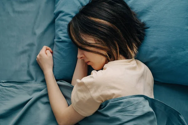 Uma jovem dorme em uma cama com roupa de cama azul. — Fotografia de Stock