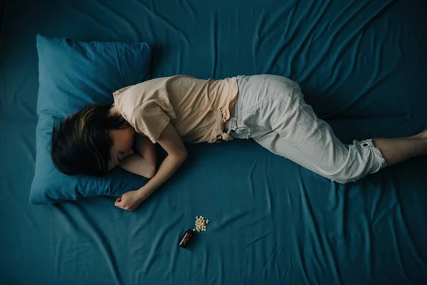 Ovanifrån av en ung kvinna i sängen med piller som ligger bredvid henne. — Stockfoto