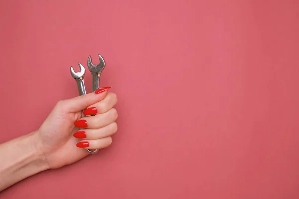 Mão feminina com uma manicura vermelha e uma chave inglesa sobre um fundo vermelho. — Fotografia de Stock