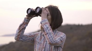 Genç kadın dürbünle bakar ve dağ manzarasına hayran kalır..