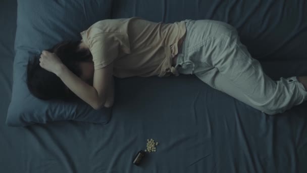 Uma mulher deita-se na cama com as mãos na cabeça. Cefaleias ou enxaqueca conceito. — Vídeo de Stock