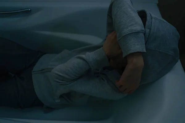 Молодая женщина в капюшоне сидит в ванной и закрывает лицо руками.. — стоковое фото