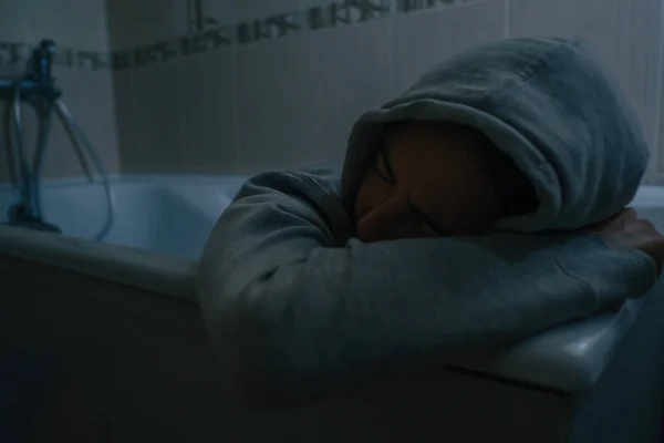 Расстроенная женщина в одежде лежит в ванной комнате. — стоковое фото