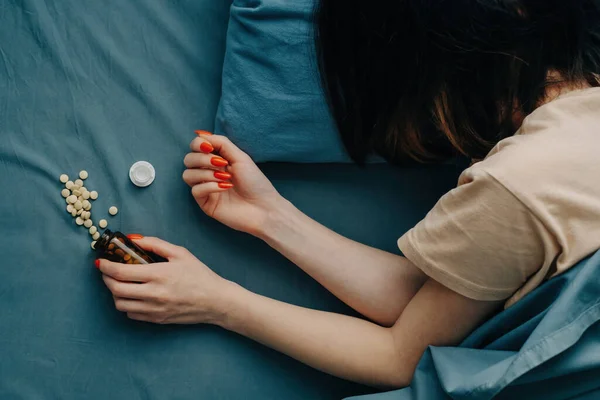 Ovanifrån av en ung kvinna i sängen med spridda piller i närheten. — Stockfoto
