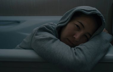 Depresyonda olan üzgün bir kadın banyoda kıyafetlerle yatıyor..