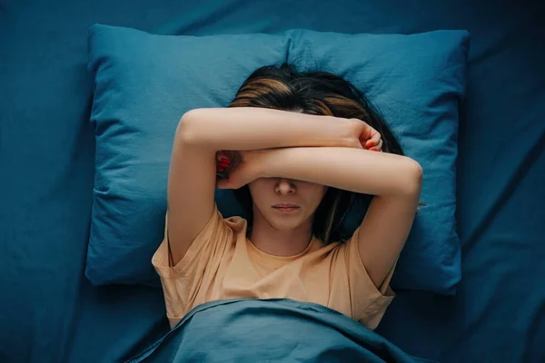 Eine Frau mit Kopfschmerzen oder Migräne liegt im Bett. — Stockfoto