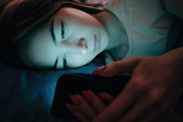 Genç bir kadın gece telefonundan sosyal ağları izliyor ya da bir mesaja cevap veriyor.. — Stok fotoğraf