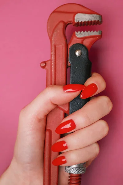 Mano femenina con clavos rojos sosteniendo una llave de fontanería. — Foto de Stock