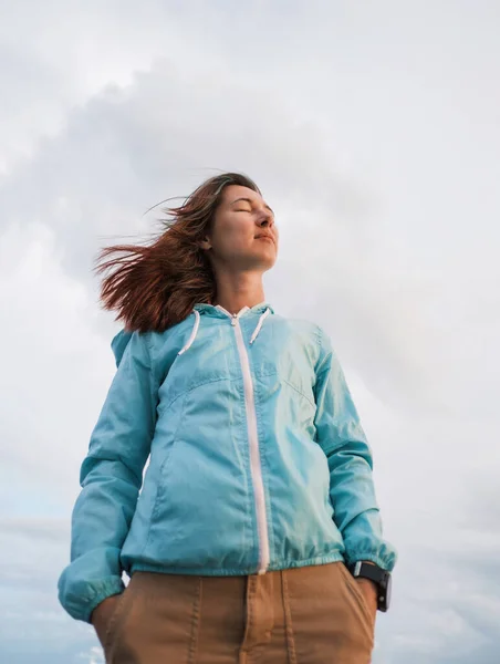 Retrato de una mujer joven en un cortavientos azul en tiempo ventoso. —  Fotos de Stock