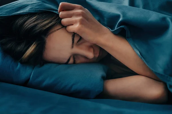 Крупним планом обличчя жінки, яка лежить в ліжку, її голова ховається під обкладинками . — стокове фото